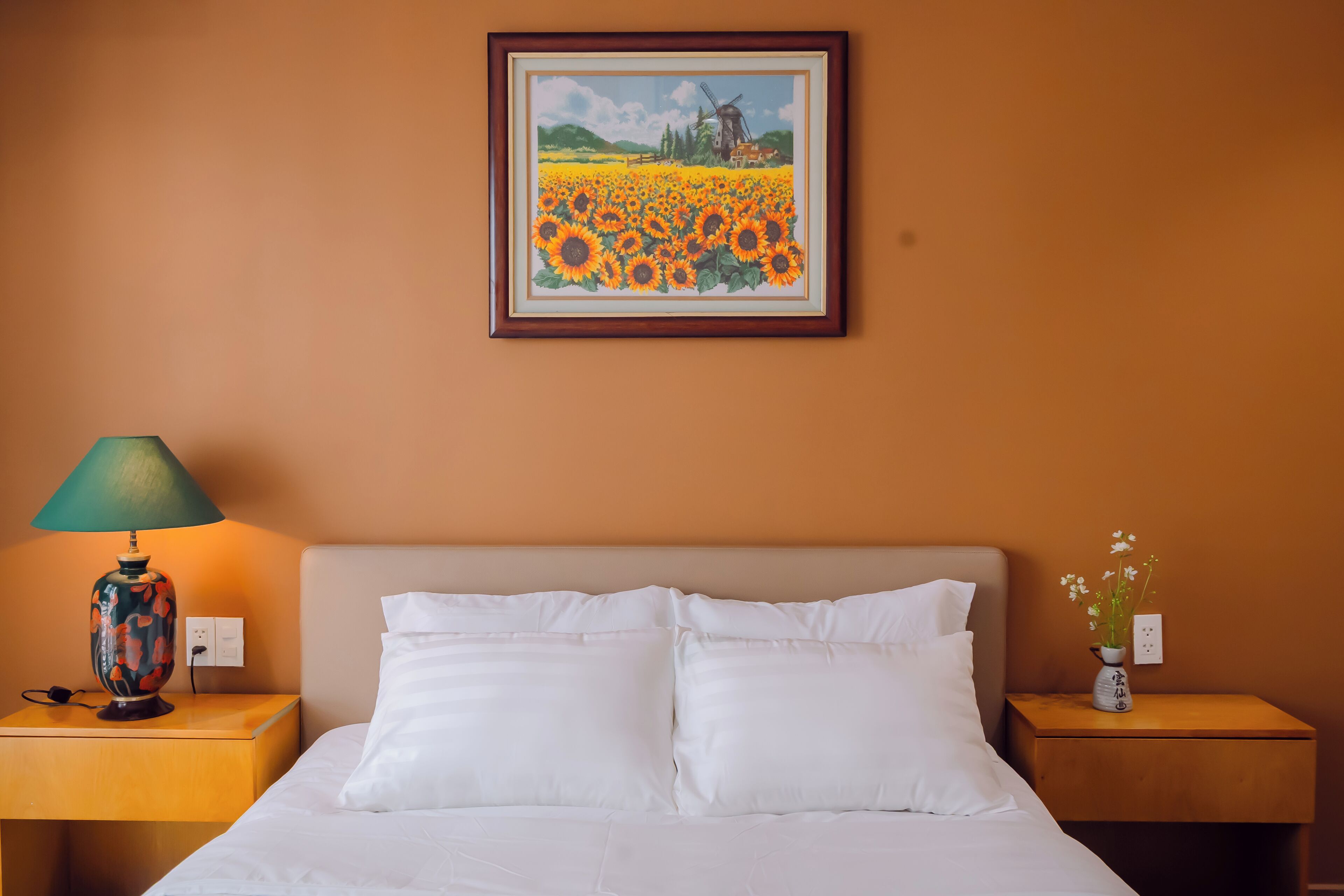 A hotel room with a bed, two nightstands, a lamp, a framed painting, and a vase with flowers.