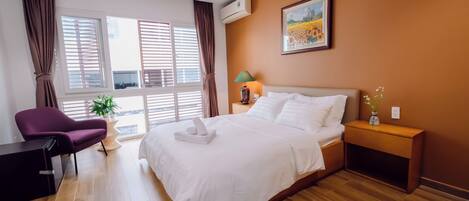 A hotel room with a bed, a desk, a chair, a nightstand, a lamp, and a window with curtains.