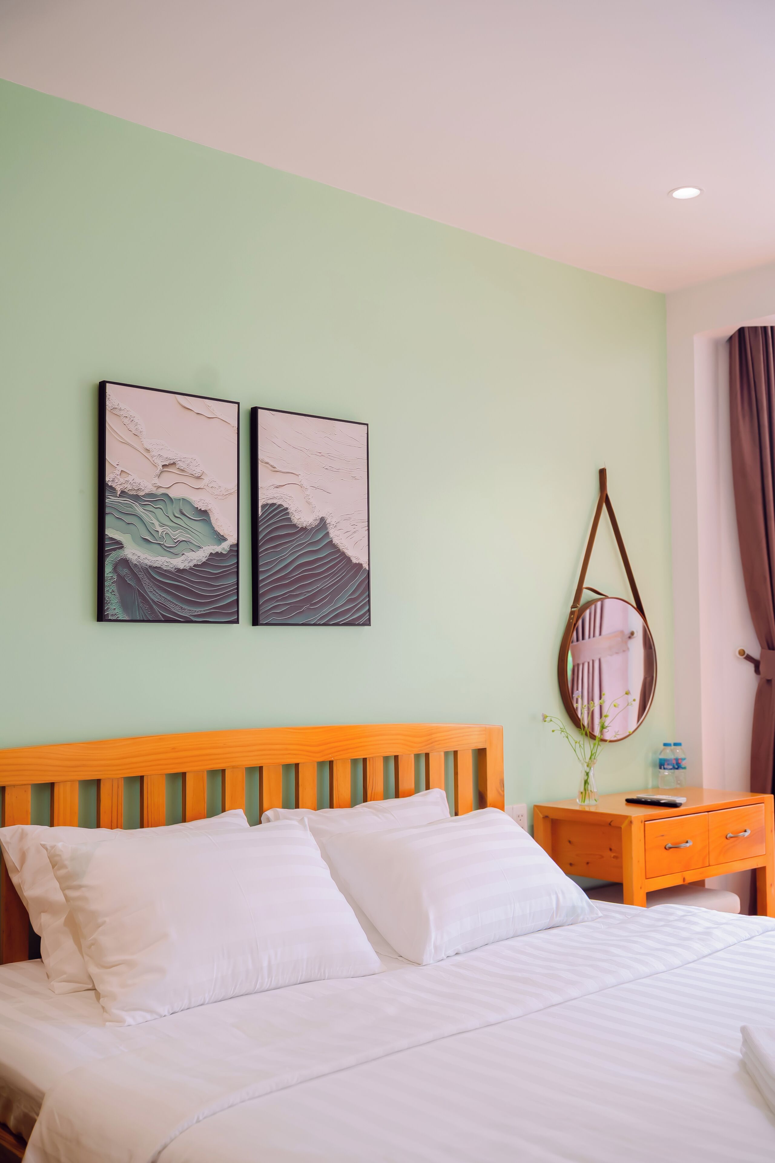 Un lit bien fait, avec du linge de lit blanc, une tête de lit en bois et deux œuvres d’art accrochées au mur représentant des vagues.