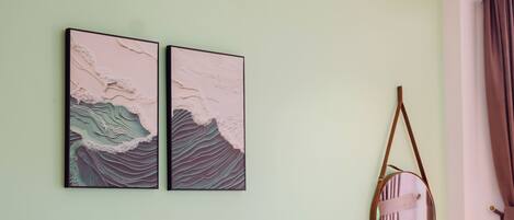 Un lit bien fait, avec du linge de lit blanc, une tête de lit en bois et deux œuvres d’art accrochées au mur représentant des vagues.