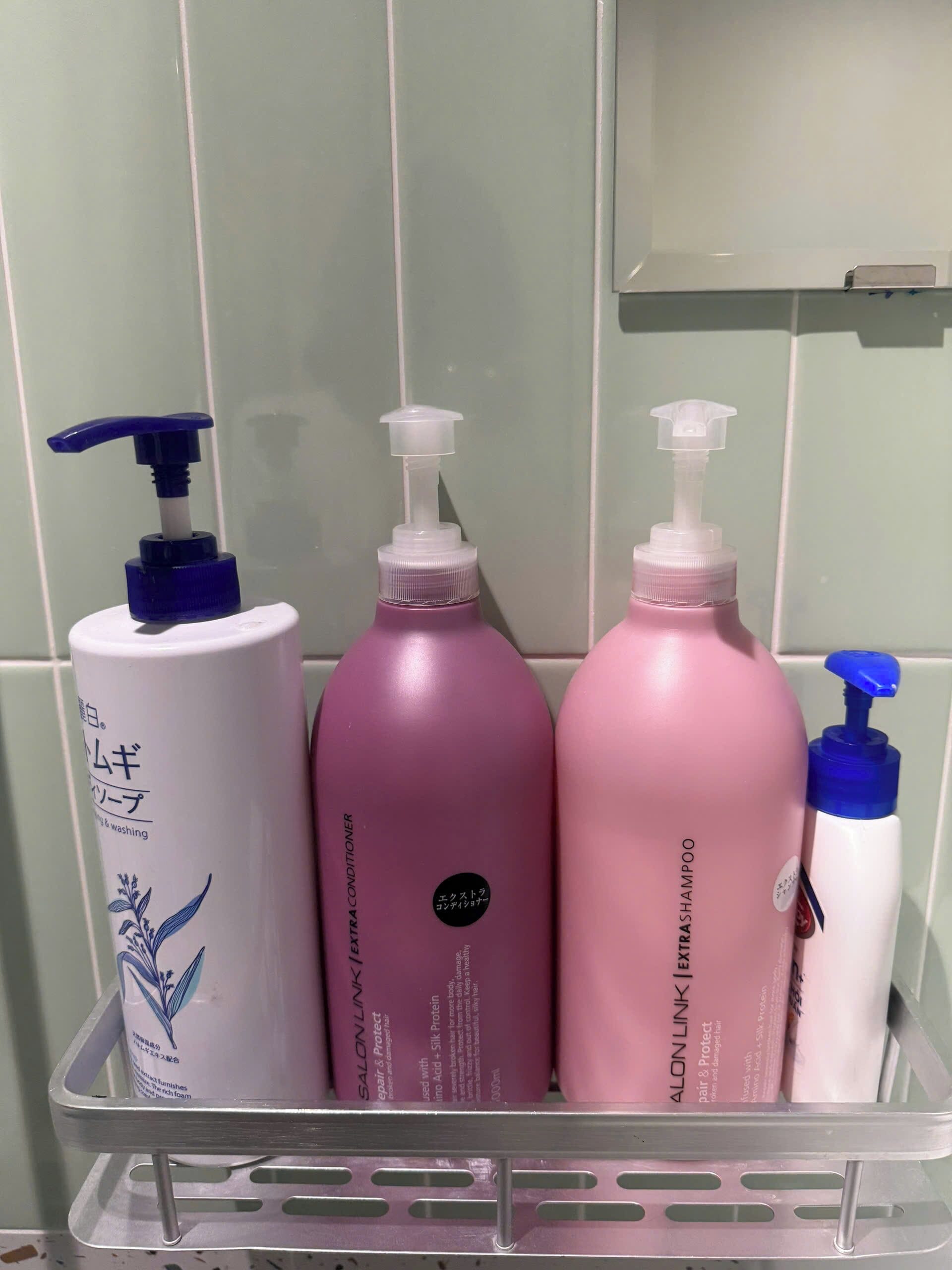 Une étagère de salle de bain avec trois flacons de produits capillaires et un récipient blanc.