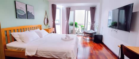 A modern hotel room with a wooden bed, a flat-screen TV, and a balcony with curtains.