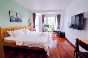 A modern hotel room with a wooden bed, a flat-screen TV, and a balcony with curtains.