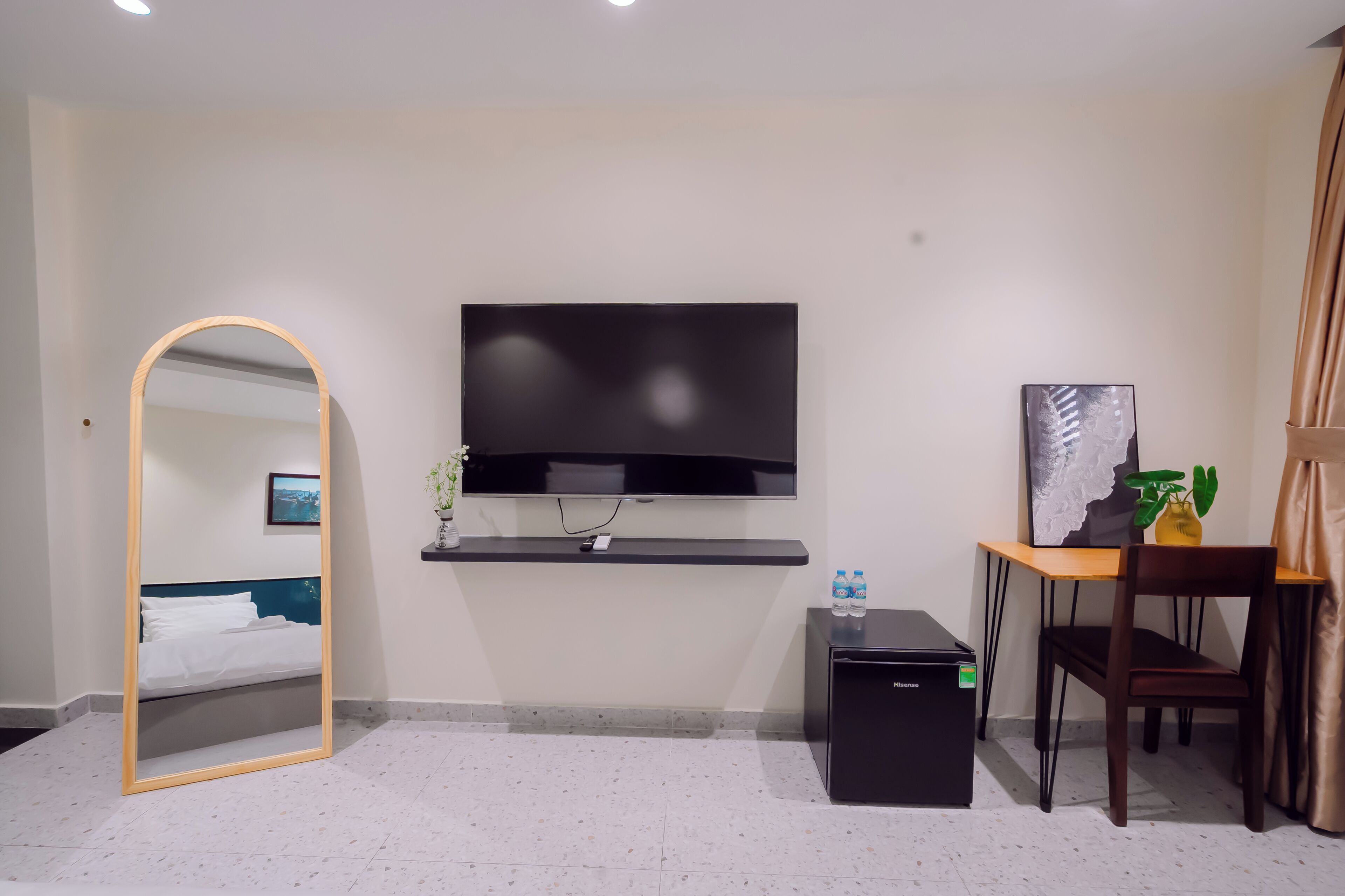 Habitación de hotel con cama, televisor montado en la pared, escritorio con silla y un mueble pequeño.