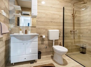 A modern bathroom with a white vanity, a toilet, and a glass-enclosed shower. - Villa Peace Oasis (Lovreć)