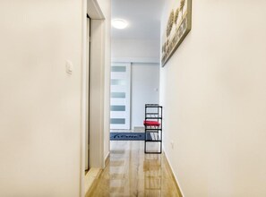 A hallway with a door, a wall-mounted shelf with a red cushion, and a framed picture.