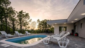 A modern outdoor pool area with lounge chairs and a building with a flat roof. - Villa Peace Oasis (Lovreć)