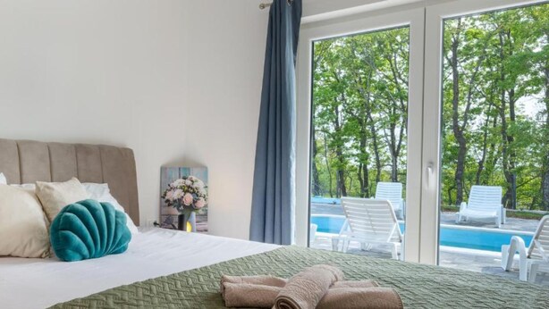 A hotel room with a bed, a view of a swimming pool, and a large window. - Villa Peace Oasis (Lovreć)
