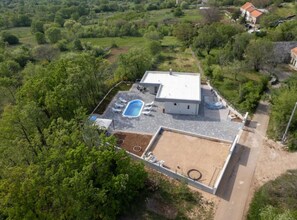 An aerial view of a house with a swimming pool, a patio, and a fenced yard.