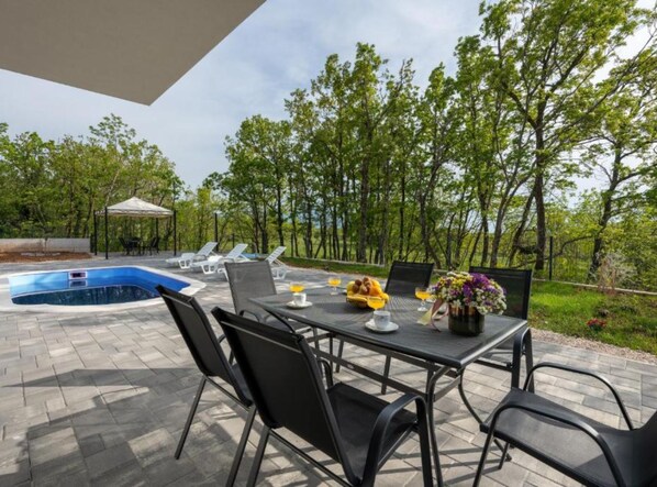 An outdoor dining area with a pool, chairs, and a table set for two.