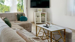 A living room with a sofa, a coffee table, a TV, and a white shelf with decorative items. - Villa Peace Oasis (Lovreć)