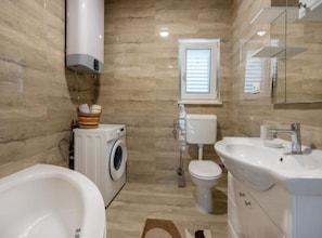 A bathroom with a washing machine, toilet, sink, and a large mirror.