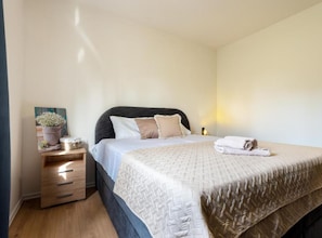 Een slaapkamer met een bed, nachtkastje en een foto aan de muur.