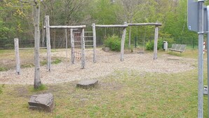 Un parque infantil con columpios y una estructura para escalar, rodeado de árboles y una valla.