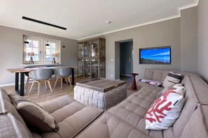 Een moderne woonkamer met een bank, een voetenbankje, een eettafel met stoelen, een kast en een televisie.