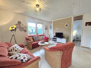 Uma sala de estar com sofá, mesa de centro, televisão e área de jantar.