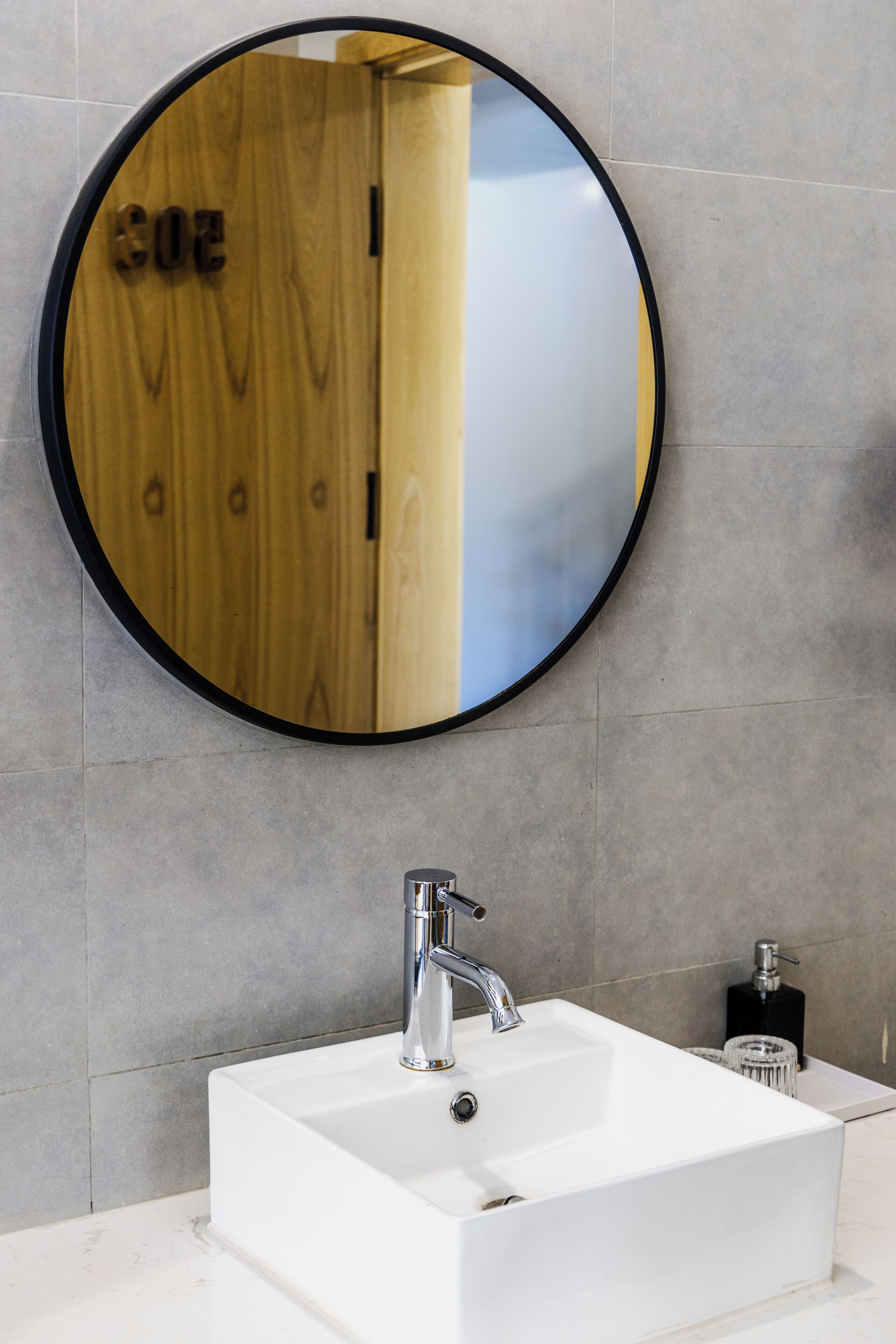 Un baño con un espejo redondo, un lavabo blanco y una puerta de madera.