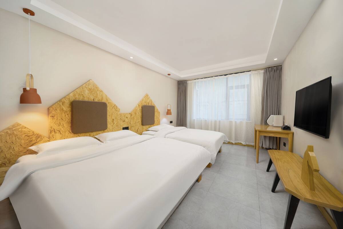 A hotel room with two beds, a TV, a desk, and a window with curtains.
