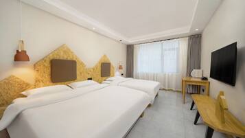 A hotel room with two beds, a TV, a desk, and a window with curtains.