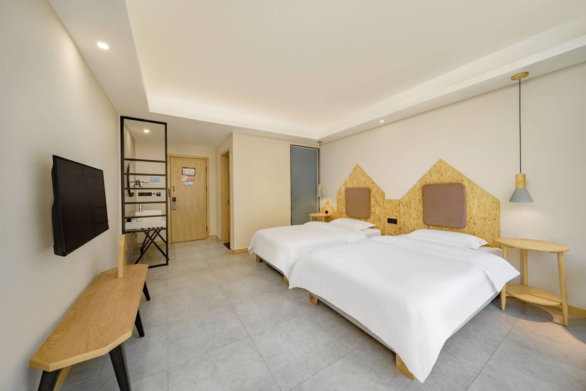 A hotel room with two beds, a desk, a TV, and a mirror.