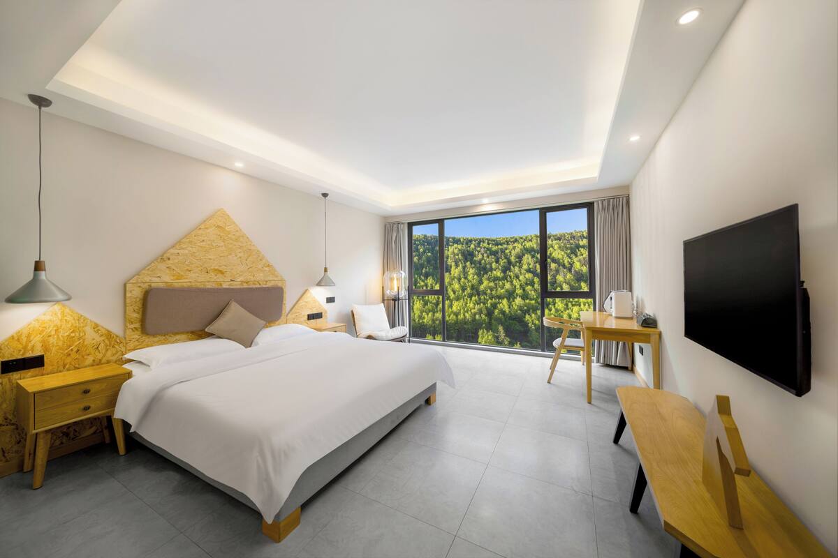 A modern hotel room with a large bed, a desk, a TV, and a scenic view through the windows.