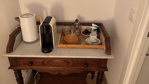 Un comptoir de cuisine avec une machine à café, une bouilloire, un plateau avec des tasses et une théière, ainsi qu’une table en bois dotée de tiroirs.