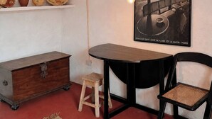Ett rum med ett skrivbord i trä, en stol, en liten pall, en hängande lampa och en affisch som hänger på väggen.