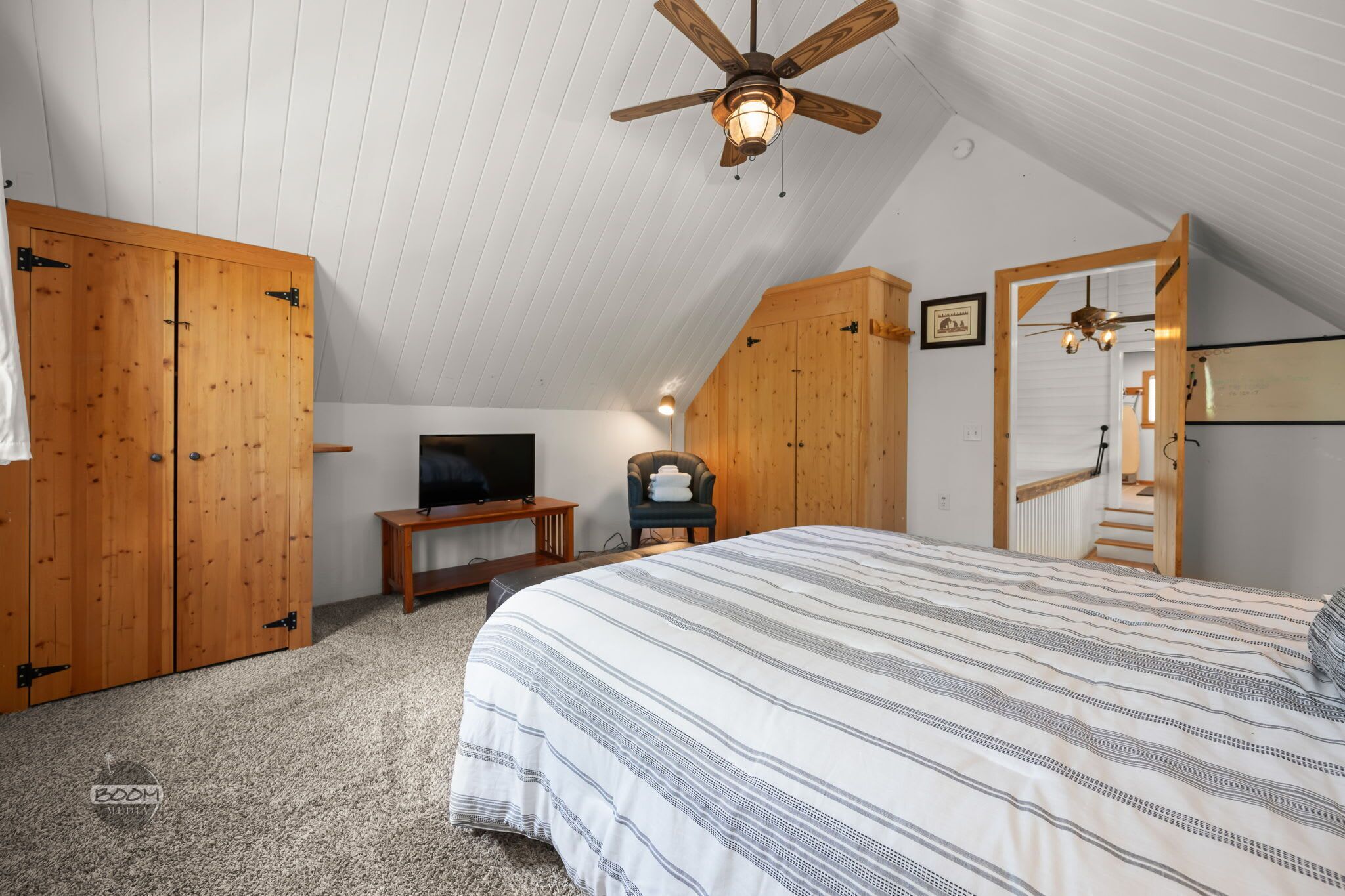 A bedroom with a bed, wooden wardrobe, television, and a ceiling fan.