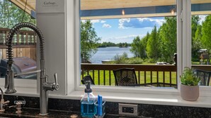 A kitchen with a view of a lake, a sink with a faucet, and a sign advising not to put food in the sink. - Lakeside Retreat- Charming 5 Bedroom, with Kayaks! (Wasilla)