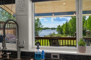 A kitchen with a view of a lake, a sink with a faucet, and a sign advising not to put food in the sink.