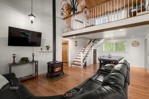 A spacious living room with a fireplace, a television, a staircase to an upper level, and a dining area.
