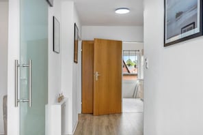 A hallway with a glass shower enclosure, wooden doors, and a view of a balcony with a railing.