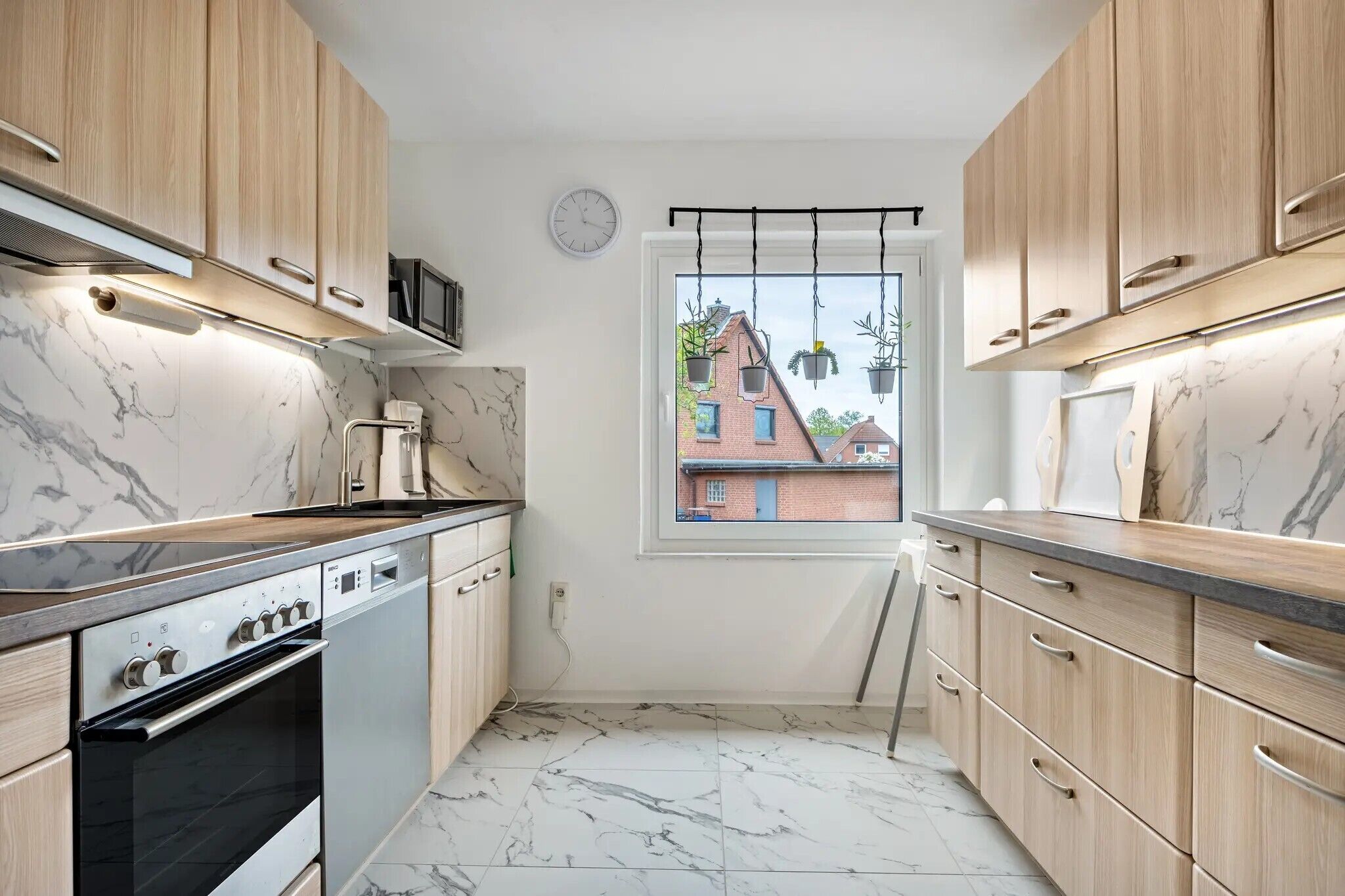 A compact kitchen with wooden cabinets, a built-in oven, and a window with a view of buildings.