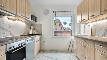 A compact kitchen with wooden cabinets, a built-in oven, and a window with a view of buildings.