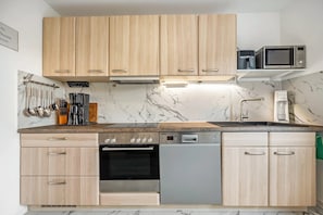 Une cuisine moderne avec des meubles en bois, un four encastré, un lave-vaisselle et un micro-ondes posé sur une étagère.