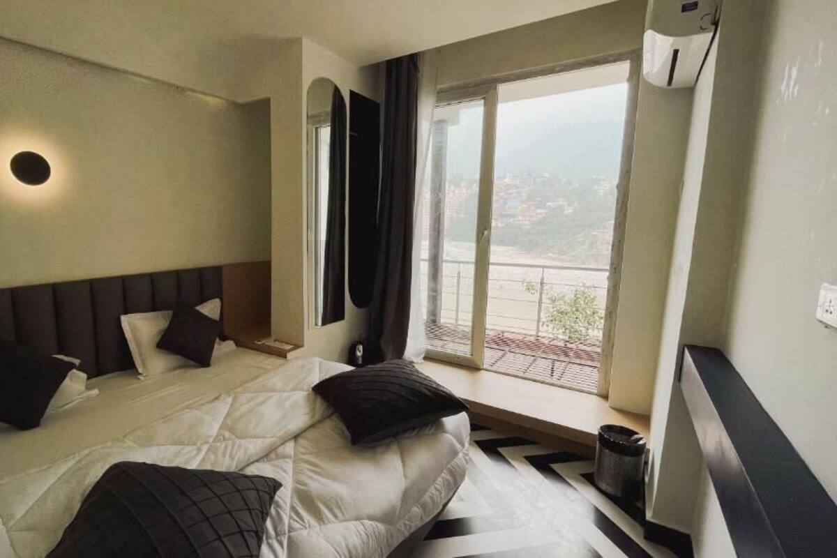 A hotel room with a bed, a window with a view, a wall-mounted air conditioning unit, and a small table.