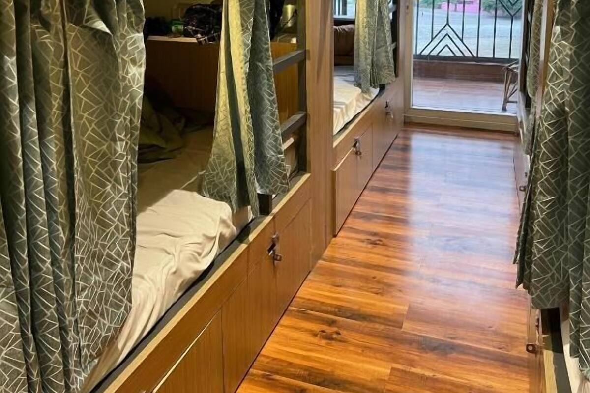 A bunk bed room with a wooden floor, a balcony with a view, and curtains with a geometric pattern.