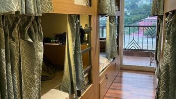 A bunk bed room with a wooden floor, a balcony with a view, and curtains with a geometric pattern.