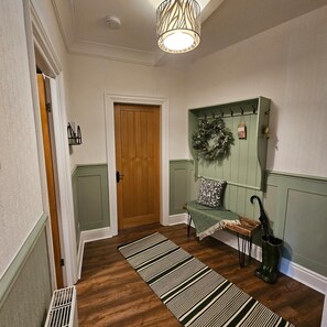 A hallway with a wooden door, a bench with a green cushion, a hanging wreath, and a striped rug. - Park View Penthouse Suite (Merseyside)
