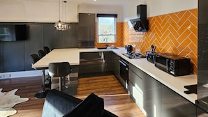 A modern kitchen with a dining area, a large island, and a TV mounted on the wall. - Park View Penthouse Suite (Merseyside)