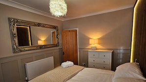 A bedroom with a large bed, a dresser, a mirror, a radiator, and a ceiling light fixture. - Park View Penthouse Suite (Merseyside)