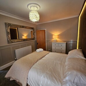 A bedroom with a large bed, a dresser, a mirror, a radiator, and a ceiling light fixture. - Park View Penthouse Suite (Merseyside)