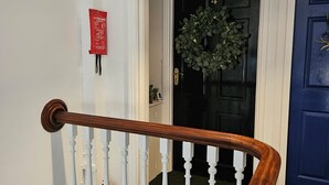 A staircase with white balusters and a wooden handrail, leading to a black door with a wreath. - Park View Penthouse Suite (Merseyside)