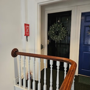 A staircase with white balusters and a wooden handrail, leading to a black door with a wreath. - Park View Penthouse Suite (Merseyside)