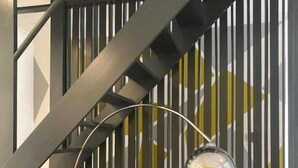 Un interno moderno con una scala, due poltrone color acquamarina con cuscini gialli, un tavolino rotondo e una lampada da terra.