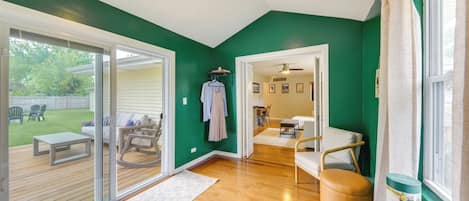 A room with a wooden floor, a ceiling fan, a sliding glass door leading to an outdoor area, and a window with curtains.