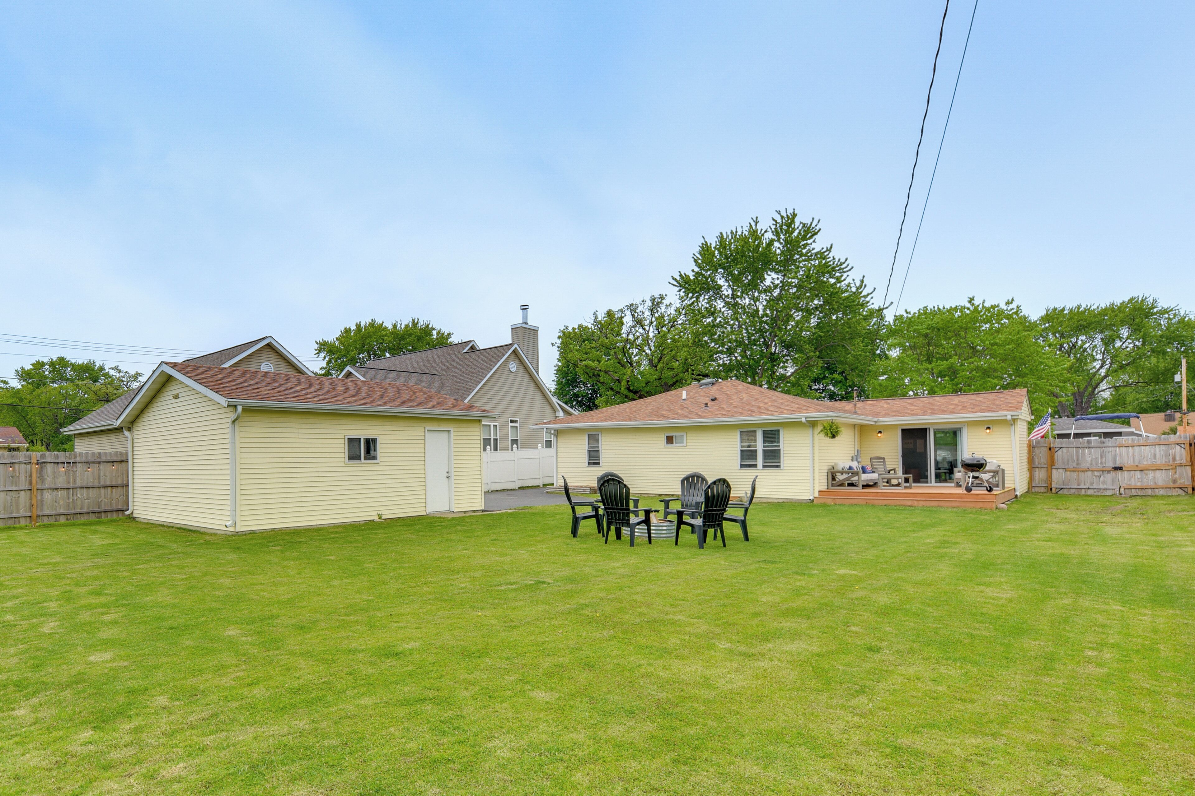 A residential backyard with a house, a patio with chairs, and a small shed.