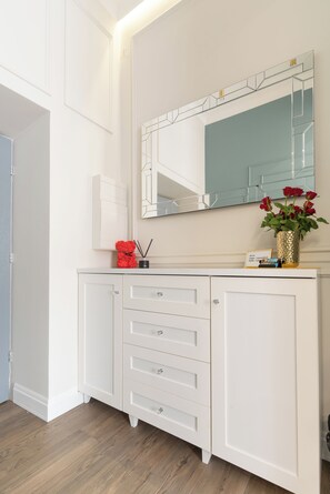 Ein weißer Schminktisch mit Schubladen, einem Spiegel und einer Vase mit roten Blumen.