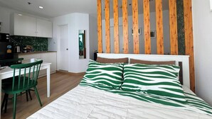 Une chambre à coucher avec un lit, des oreillers à rayures vertes et blanches, une tête de lit en bois, une table de chevet blanche et une chaise verte.