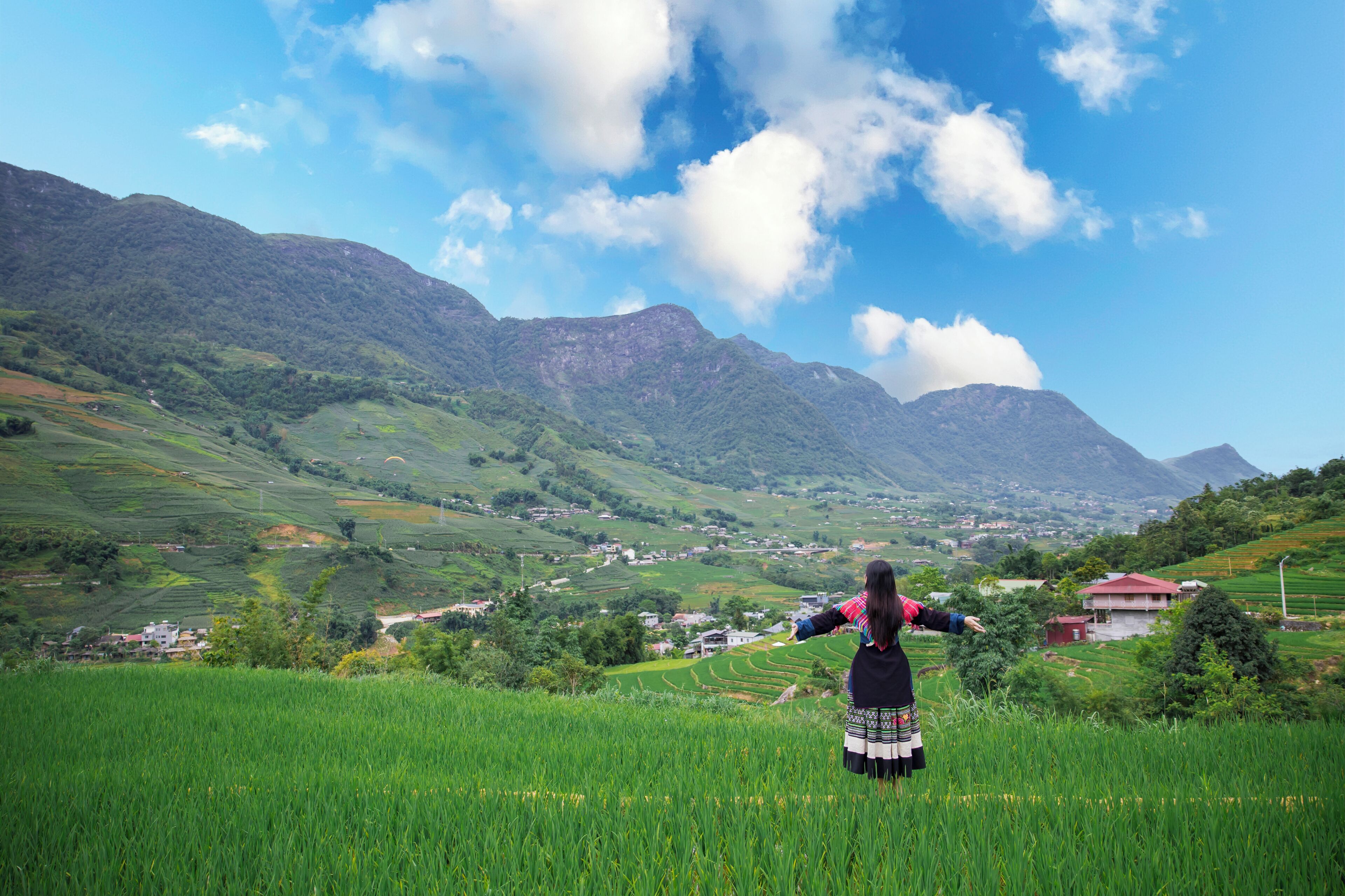 Una persona de pie en un campo verde con montañas al fondo.